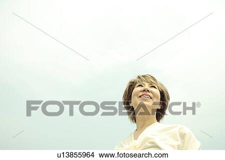 Picture - Mature woman smiling under sky, copy space. Fotosearch