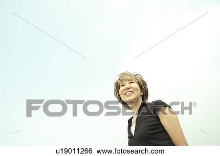 Stock Photograph - Mature woman smiling under sky, copy space. Fotosearch