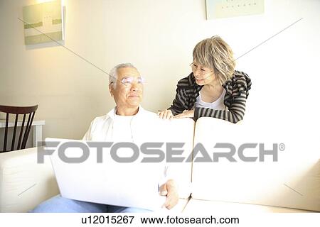 Mature woman talking to senior man using laptop on sofa View Large Photo Image Stock Photo - Mature woman talking to senior man using laptop on sofa. Fotosearch