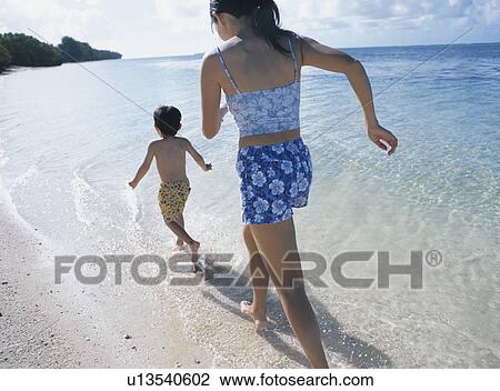 Stock Image - Mother and son running on beach. Fotosearch