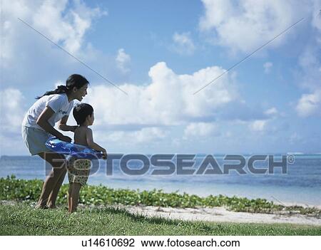 Stock Image - Mother and son standing on beach, Saipan, USA. Fotosearch