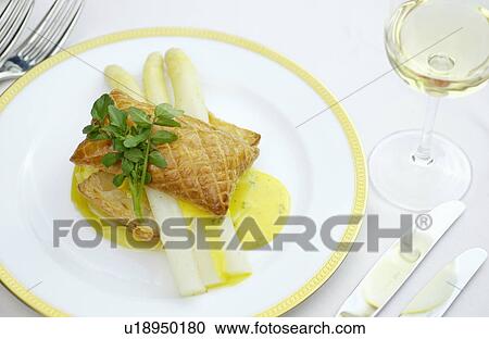 Stock Image - Plate of asparagus and puff pastry on table, white background. Fotosearch