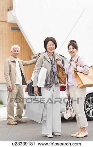 Stock Image - Portrait of family holding shopping bags, senior man standing by car, smiling. Fotosearch