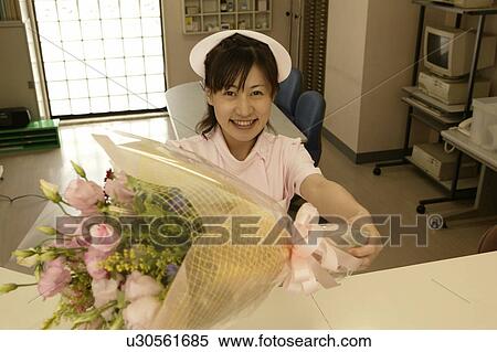 Stock Photography - Portrait of female nurse holding flower bouquet, smiling. Fotosearch