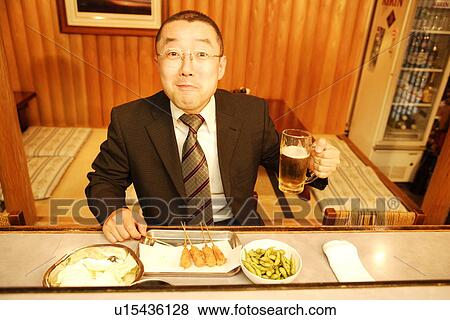 Stock Photo - Portrait of mature man sitting at bar counter, holding glass of beer. Fotosearch