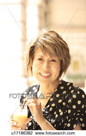 Stock Image - Portrait of mature woman holding glass, smiling. Fotosearch