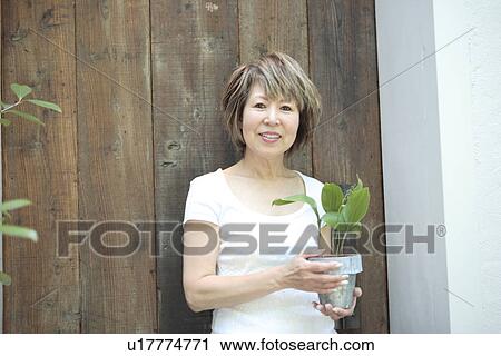 Stock Image - Portrait of mature woman holding potted plant, smiling. Fotosearch