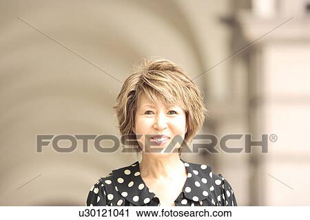 Stock Image - Portrait of mature woman in arcade, smiling, differential focus. Fotosearch