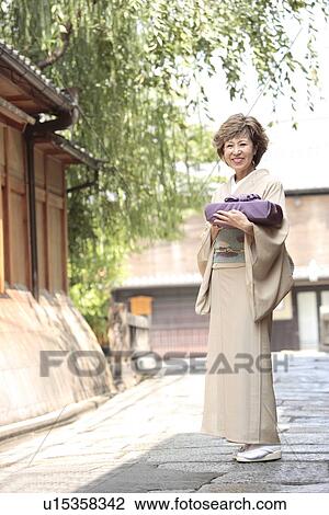 Stock Image - Portrait of mature woman in Kimono holding gift, Kyoto city, Kyoto prefecture, Japan. Fotosearch
