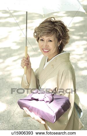 Stock Image - Portrait of mature woman in Kimono holding umbrella and gift, Kyoto city, Kyoto prefecture, Japan. Fotosearch