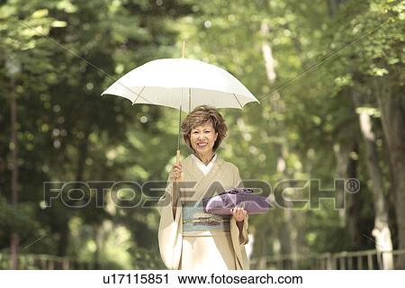 Stock Image - Portrait of mature woman in Kimono holding umbrella and gift, Kyoto city, Kyoto prefecture, Japan. Fotosearch