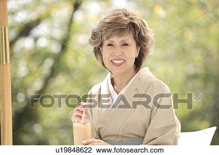 Stock Image - Portrait of mature woman in Kimono sitting at cafe table, differential focus, Kyoto city, Kyoto prefecture, Japan. Fotosearch