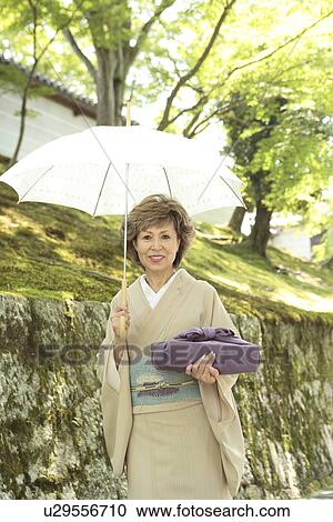 Stock Image - Portrait of mature woman in Kimono holding umbrella and gift, Kyoto city, Kyoto prefecture, Japan. Fotosearch