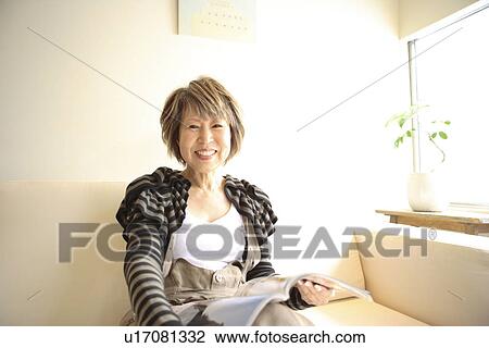 Portrait of mature woman sitting on sofa, holding magazine View Large Photo Image Stock Image - Portrait of mature woman sitting on sofa, holding magazine. Fotosearch