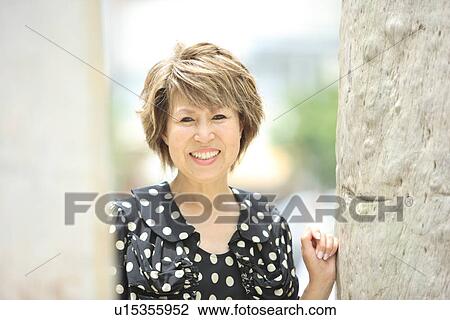 Portrait of mature woman standing by tree trunk, smiling View Large Photo Image Stock Image - Portrait of mature woman standing by tree trunk, smiling. Fotosearch