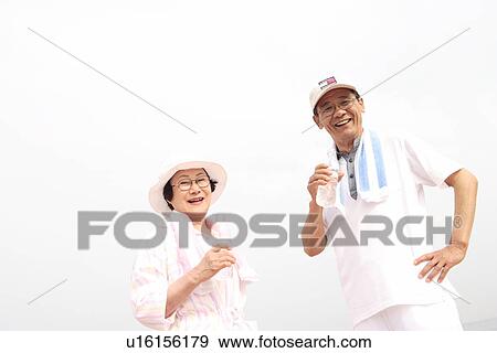 Stock Photo - Portrait of senior couple holding bottles of water, smiling. Fotosearch