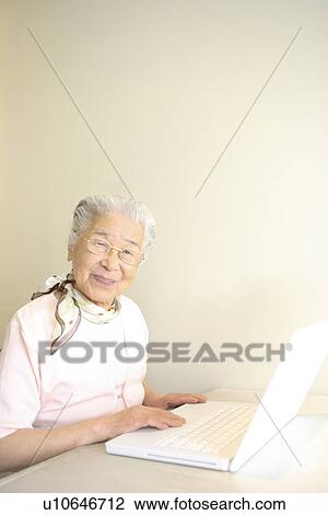 Stock Image - Portrait of senior woman using laptop, smiling, white background. Fotosearch