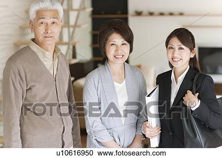 Stock Image - Portrait of young businesswoman and senior couple in living room, smiling. Fotosearch