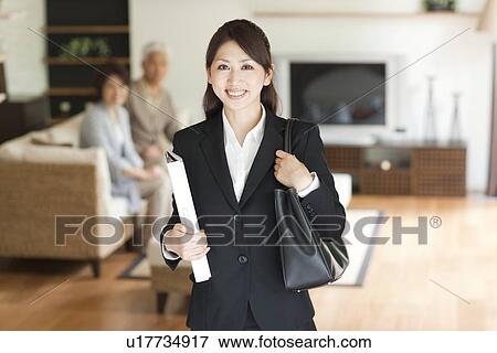 Portrait of young businesswoman in living room, senior couple sitting on sofa in background, differential focus View Large Photo Image Stock Photo - Portrait of young businesswoman in living room, senior couple sitting on sofa in background, differential focus. Fotosearch