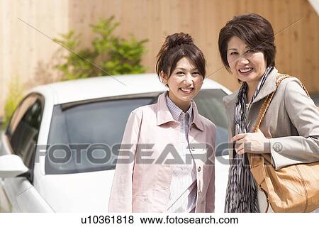 Stock Photo - Portrait of young woman and senior woman standing by car, smiling. Fotosearch