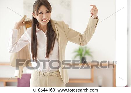 Stock Image - Portrait of young woman putting on jacket, smiling. Fotosearch