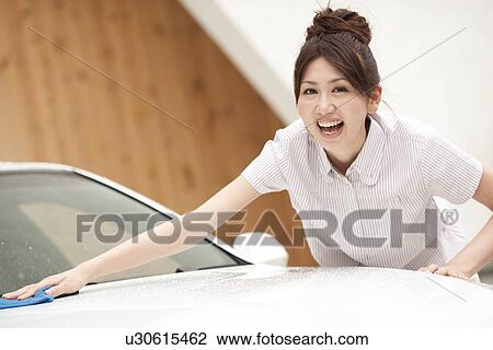 Stock Image - Portrait of young woman washing car, smiling. Fotosearch