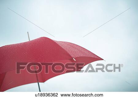Stock Image - Red umbrella in rainy sky, blue background. Fotosearch