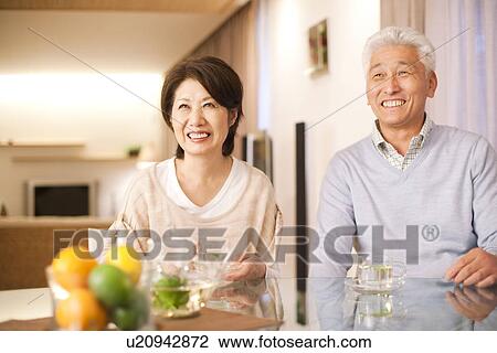 Stock Image - Senior couple drinking tea at dining table, smiling. Fotosearch