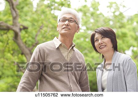 Stock Image - Senior couple in woods, smiling and looking up. Fotosearch