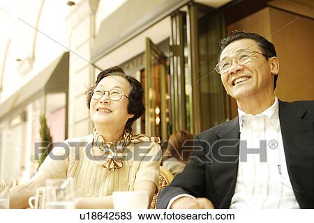 Stock Image - Senior couple sitting at table in cafe, smiling. Fotosearch