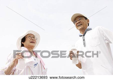 Senior couple smiling under sky, man holding bottle of water View Large Photo Image Stock Image - Senior couple smiling under sky, man holding bottle of water. Fotosearch