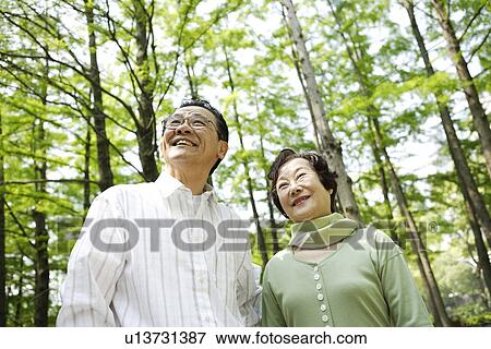 Stock Photo - Senior couple standing under trees, smiling. Fotosearch