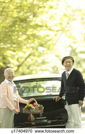Stock Image - Senior couple taking out a basket full of fruits and vegetables from car trunk. Fotosearch