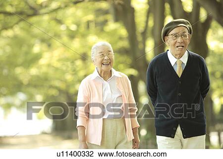 Stock Image - Senior couple walking treelined street. Fotosearch