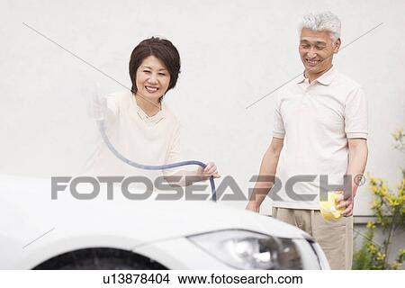 Picture - Senior couple washing car, using hose and sponge. Fotosearch