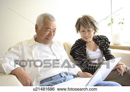 Stock Photograph - Senior man and mature woman looking at laptop monitor on sofa, smiling. Fotosearch