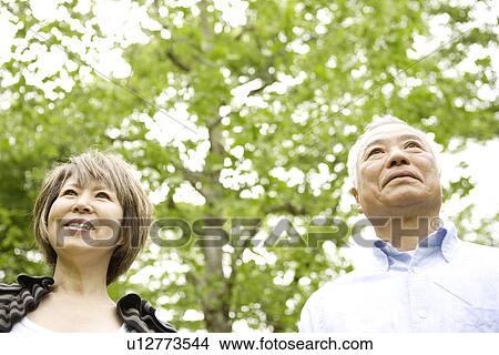Senior man and mature woman standing under trees, smiling View Large Photo Image Picture - Senior man and mature woman standing under trees, smiling. Fotosearch