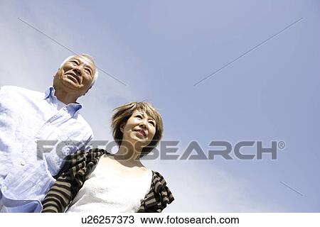 Stock Image - Senior man and mature woman standing under blue sky, copy space. Fotosearch