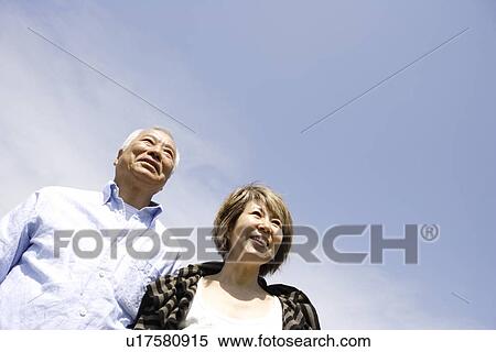 Stock Photography - Senior man and mature woman standing under blue sky, copy space. Fotosearch