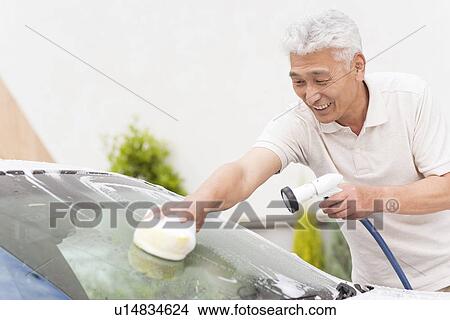 Picture - Senior man washing car, holding hose and sponge. Fotosearch