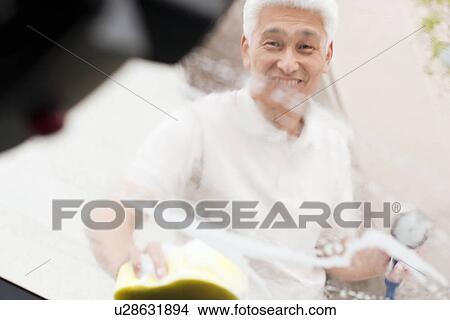 Picture - Senior man washing car, holding hose and sponge. Fotosearch