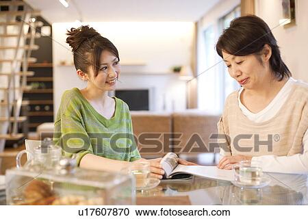 Stock Image - Senior woman and young woman reading magazine at dining table. Fotosearch