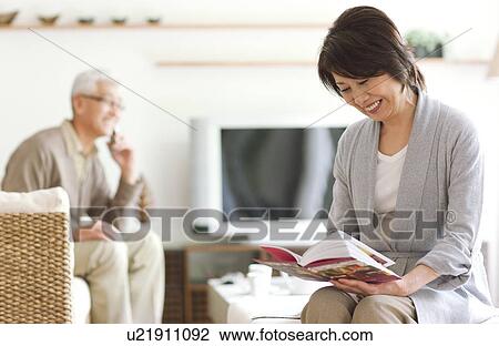 Stock Image - Senior woman reading a book and senior man on cell phone. Fotosearch