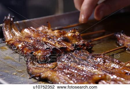 Stock Image - Slices of eel being grilled on barbecue, close up. Fotosearch