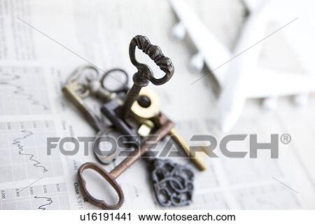 Stock Image - Stack of keys and toy airplane on newspaper, close up. Fotosearch