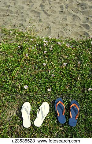 Stock Image - Two pairs of sandals on beach. Fotosearch