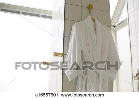 Stock Image - White bathrobes hanging on tiled wall. Fotosearch