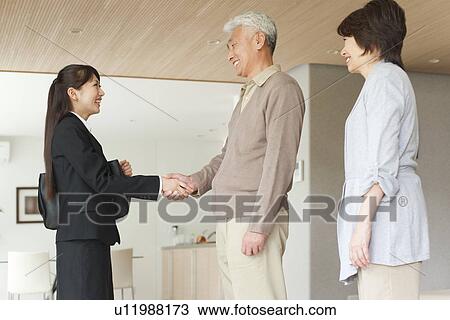 Stock Image - Young businesswoman and senior man shaking hands, smiling. Fotosearch