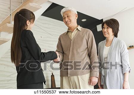 Stock Photo - Young businesswoman and senior man shaking hands, smiling. Fotosearch
