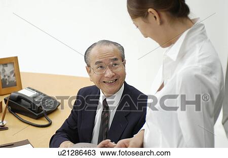 Stock Image - Young Woman Executive Assistant and Her Boss at Office. Fotosearch